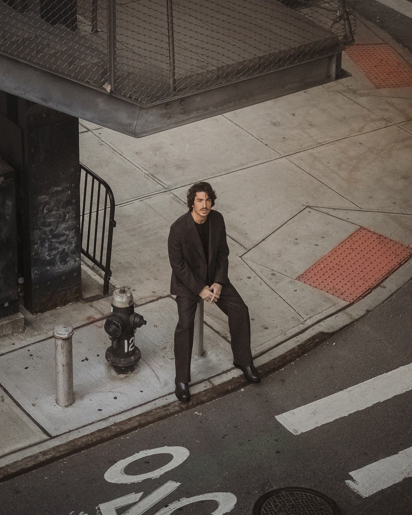 Rafael Gasparini sentado em cenário urbano para Zegna AW24 com styling de Michael Juvêncio